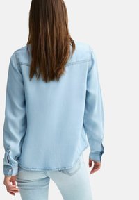 Camicia in denim blu chiaro con maniche lunghe, polsini a bottone e giromanica sul retro. Tessuto morbido con una consistenza liscia e una vestibilità casual.