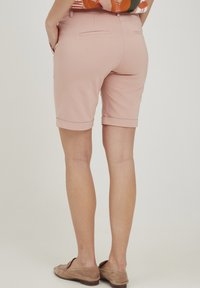 Rozā ceļa garuma šorti ar salocītām piedurknēm, kas izgatavoti no gludas auduma un aprīkoti ar divām aizmugurējām kabatām, kopā ar beidzīgiem loafers.