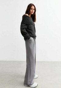 Grå off-shoulder stickad tröja med ribbad halsringning, i kombination med ljusgrå vida byxor och vita sneakers. Släta texturer genom hela outfiten.