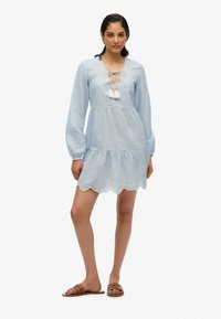 Vestido de rayas azul claro con mangas largas, dobladillo en forma de concha y un escote con abertura atado con borlas. Se lleva con sandalias planas marrones.