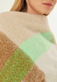 Écharpe en laine à carreaux beige et marron avec un accent vert vif. Texture douce et design douillet, présentant un style enveloppant pour plus de chaleur.