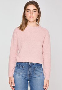 Maglione cropped rosa chiaro in morbido materiale a maglia con scollatura a girocollo e maniche lunghe, abbinato a jeans blu a vita alta con tasche a toppa.