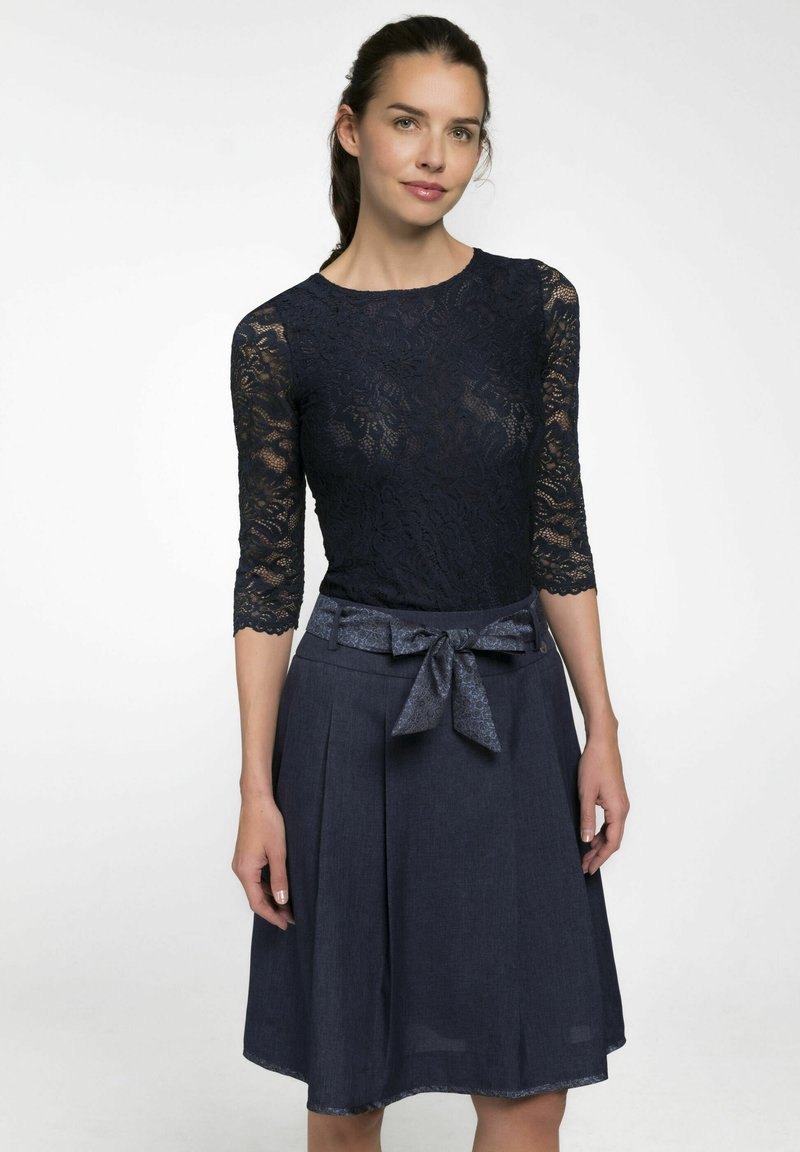 Marinebluse mit Dreiviertelärmeln, kombiniert mit einem plissierten Jeansrock, der einen passenden Stoffgürtel mit einer Schleifenapplikation hat.