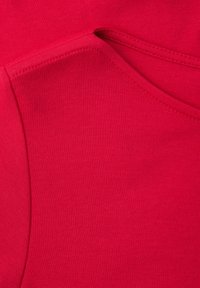 Felrood textiel met zichtbare naad en stiksels, die de gebogen rand van de halslijn van een kledingstuk benadrukken.