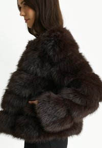 Dark brown faux fur jacket with a boxy shape, featuring thick, plush texture and wide sleeves. Notable for its layered design.