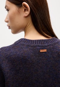 Strickpullover in dunklen Blautönen und Braun, mit einem gerippten Rundhalsausschnitt und einem kleinen Leder-Brandlabel auf der Rückseite.