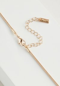 Gold-tone necklace featuring a slender, twisted chain, a lobster clasp, and an adjustable chain with a rectangular tag.
