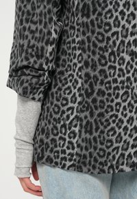 Top s černobílým leopardím potiskem vyrobený z lehkého materiálu s ohrnutými rukávy, navlečený přes světle šedou dlouhousedovou košili. Spodní část tvoří pohodlné džíny.
