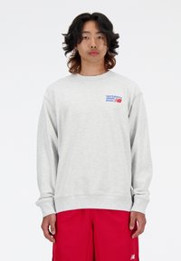 Sweat-shirt gris avec des poignets et un ourlet côtelés, arborant le logo multicolore "New Balance" sur la poitrine gauche. Tissu en mélange de coton.