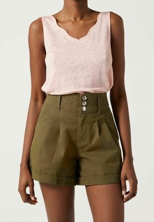 Vrouw draagt een lichtroze mouwloze top, ingestopt in olijfgroene shorts met een hoge taille, drie knopen en riemlussen.