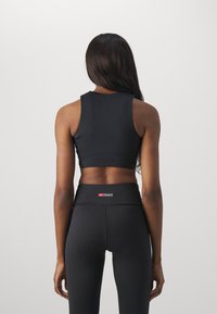 Črn športni top s visokim ovratnikom in obliko racerback, v kombinaciji z visokimi črnimi leginami, ki imajo logo na pasu.