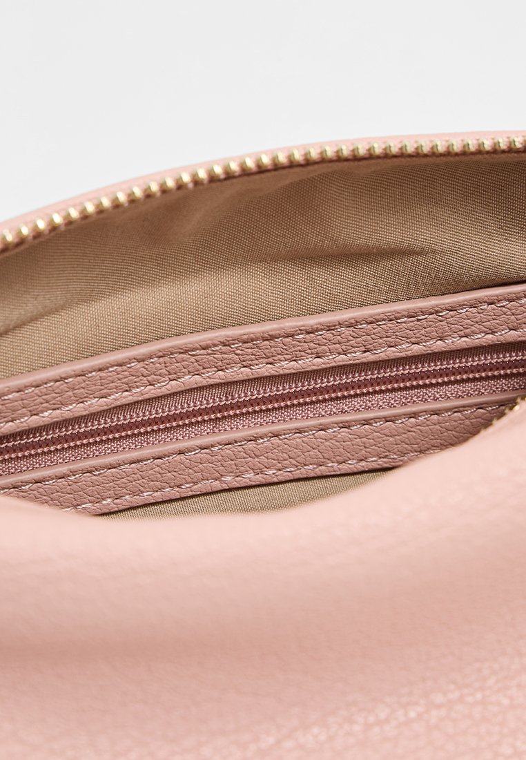 Helles rosa Kunstledertascheninnere, das eine Reißverschlusstasche mit einem glatten Reißverschluss und einer beige Stoffauskleidung aufweist. Dezente, strukturierte Oberfläche.