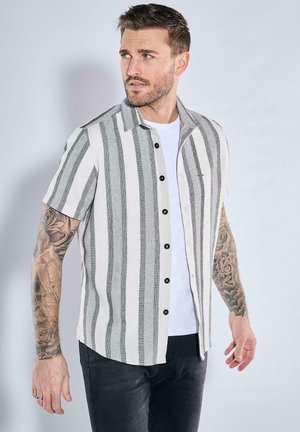 Kurzärmliges Hemd mit vertikalen grauen und weißen Streifen, Knopfleiste, aus strukturiertem Stoff gefertigt. Über einem weißen T-Shirt getragen.