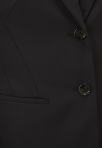 Black suit jacket fabric with a smooth texture, featuring two black buttons, a chest pocket, and tailored seams for a structured design.