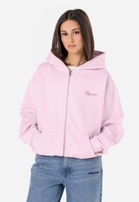 Világos rózsaszín zipzáras kapucnis pulóver, nagy kapucnival, kenguruzsebekkel és hímzett logóval. Puha anyagból készült, laza szabású, bordázott mandzsettákkal.