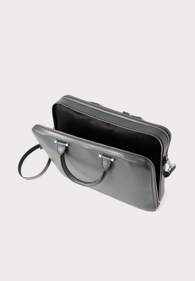 Γκρι δερμάτινη τσάντα με δομημένο σχήμα, κλείσιμο με φερμουάρ, διπλές λαβές και ευρύχωρο εσωτερικό. Λείο υλικό με ελάχιστα μεταλλικά στοιχεία.