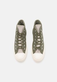 Sneakers high-top verde oliva con pannelli in rete, punte in gomma bianca e lacci a contrasto, caratterizzati da tessuto testurizzato e dettagli di cucitura.