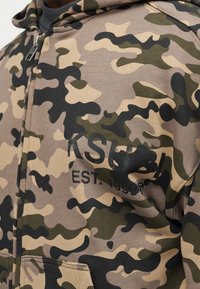 Kaptur moro na zamek w kolorach piaskowym, zielonym i czarnym. Posiada przednie kieszenie oraz napis "KSU" z rokiem założenia. Miękki materiał, casualowy krój.