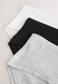 Pile de trois sous-vêtements en coton de couleur blanche, noire et gris clair, disposés en diagonale sur un fond neutre.