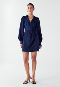 Námornícky modré zavinovacie šaty z atlasu s golierom, vypchatými dlhými rukávmi, detailom viazania na boku a ľahko drapovanou sukňou.