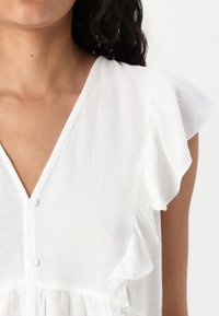 Witte linnen blouse met korte, gerimpelde mouwen, een V-halslijn en kleine knopen langs de voorkant, met een gestructureerde stof.