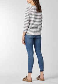 Maglia a righe grigio e bianco con maniche tre quarti, abbinata a jeans skinny blu e scarpe slip-on con motivo.