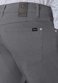 Graue gewebte Hosen mit einer strukturierten Oberfläche. Merkmale sind ein Ledergürtelschild, zwei Gesäßtaschen und silberne Metallelemente.