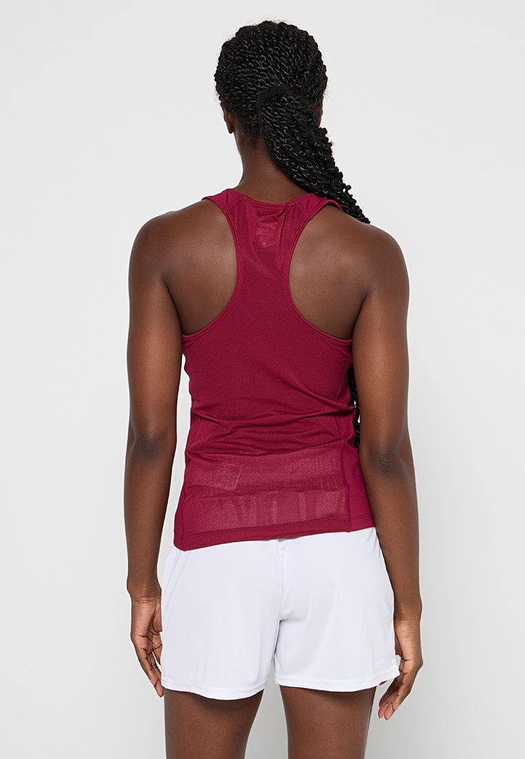Canottiera atletica bordeaux con design a schiena scoperta, caratterizzata da un tessuto testurizzato e un pannello posteriore leggermente trasparente, abbinata a pantaloni corti bianchi.