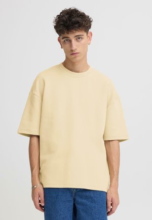 Gelbes übergroßes Baumwoll-T-Shirt mit kurzen Ärmeln und rundem Ausschnitt, kombiniert mit blauen Jeans. Einfaches und legeres Design.