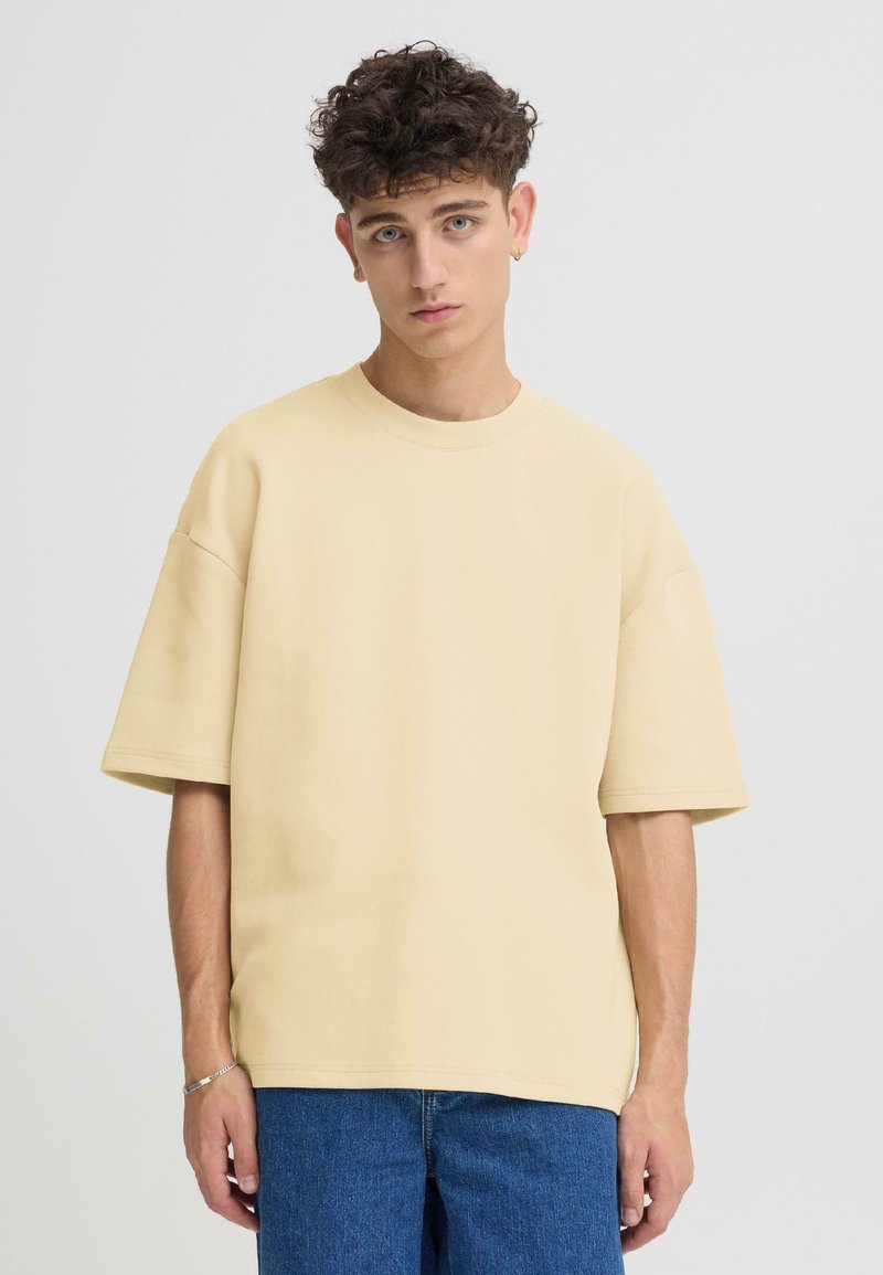 T-shirt ample en coton jaune avec manches courtes et col rond, associé à un jean en denim bleu. Design simple et décontracté.