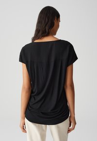 Top nero a maniche corte con vestibilità morbida, caratterizzato da un tessuto leggermente testurizzato e un collo a barca, arricciato sul retro per un maggiore drappeggio.