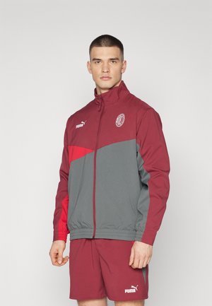 Giacca zip-up bordeaux e grigia con colletto alto, caratterizzata da un logo sul petto e pannelli colorati. Abbinata a pantaloni corto coordinati.