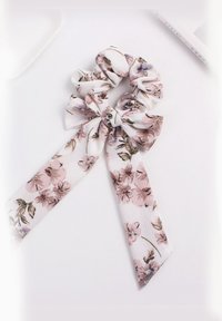 Gėlių raštas scrunchie minkštame baltoje medžiagoje, su rožinėmis ir violetinėmis gėlėmis, baigtas dviem ilgais kaspino uodegomis papildomam akcentui.