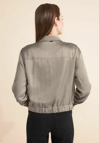 Veste en satin gris clair coupée, avec une coupe décontractée, une taille froncée et un col arrondi. Design minimaliste avec une couture arrière nette.