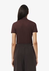 Polo marron avec une coupe ajustée, des manches courtes et un col. Associé à un pantalon sombre à taille élastique, présentant une texture lisse.