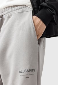 Grijze fleece joggers met elastische tailleband en zijzakken. Gedrukt "ALLSAINTS" logo op de onderlinker en een gladde, zachte textuur.