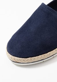 Scarpa slip-on in suede blu navy con bordo in juta intrecciata e suola in gomma bianca, caratterizzata da una superficie liscia e opaca nella parte superiore.