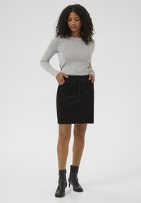 Jupe en velours côtelé noir avec une taille élastique, associée à un haut gris clair à manches longues. Des bottes noires à la cheville complètent la tenue.