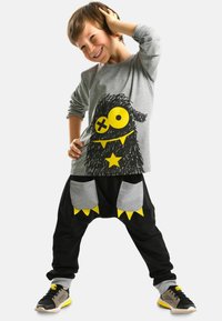 Graues Langarmshirt mit schwarzem Monster-Graphic und gelben Akzenten, kombiniert mit schwarzen weiten Hosen mit grauen Taschen und gelben Details.