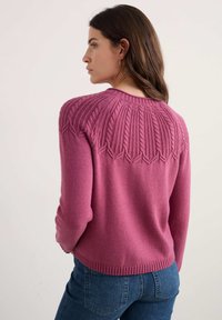 Suéter de punto rosa con un diseño texturizado en los hombros, puños acanalados y dobladillo, combinado con unos jeans de mezclilla.