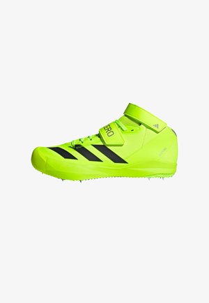 Zapatilla deportiva verde brillante con rayas negras, parte superior sintética, cierre con cordones y Velcro, puntera redondeada y suela con clavos para mayor tracción.