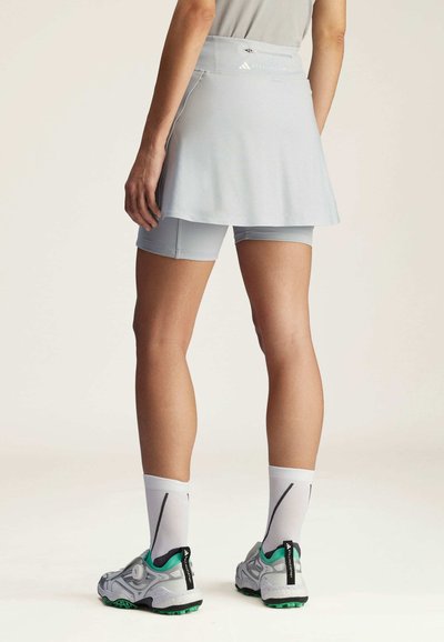 Falda-pantalón deportiva azul claro con cintura elástica, combinada con pantalones cortos a juego debajo y zapatillas deportivas grises y verdes.