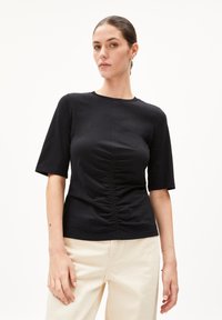 Schwarzes T-Shirt mit kurzen Ärmeln und gerafftem Detail vorne. Hergestellt aus weichem Stoff, mit rundem Ausschnitt und lockerer Passform.