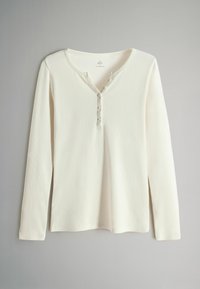 Pikkade varrukatega kreemjas värvitoonis särk, millel on ribatakistus, V-kujuline kaelus ja viis nööpi ees. Omab mugavat lõiget ja pehmet kangast.