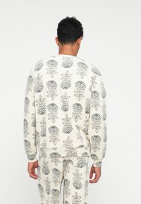 Sudadera de tela ligera, con un patrón floral en gris sobre un fondo crema. Cuello redondeado y puños acanalados.