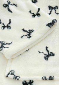 Mjuk vit fleece-tyg med ett upprepat svart rosmönster, med en slät yta och sydda kanter.