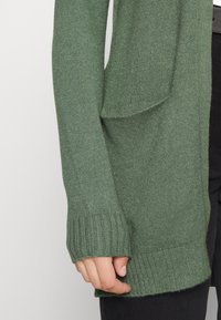 Groene gebreide cardigan met een ontspannen pasvorm, geribde manchetten en zoom, met een zak aan de voorkant en een zachte textuur.