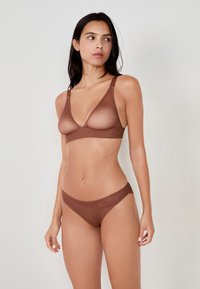 Bralette trasparente marrone con scollatura a V e spalline larghe, abbinata a slip a vita media coordinati. Texture liscia, dettagli di cucitura minimi.