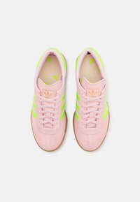 Różowe zamszowe trampki z jasnymi zielonymi paskami, gumową podeszwą i pasującym wzorem na wkładce. Posiadają wyściełany kołnierz oraz metkę z logo.