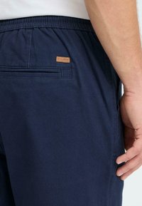 Pantalon bleu marine en tissu avec une ceinture élastique, doté d'une poche arrière et d'une petite étiquette en cuir pour la marque.